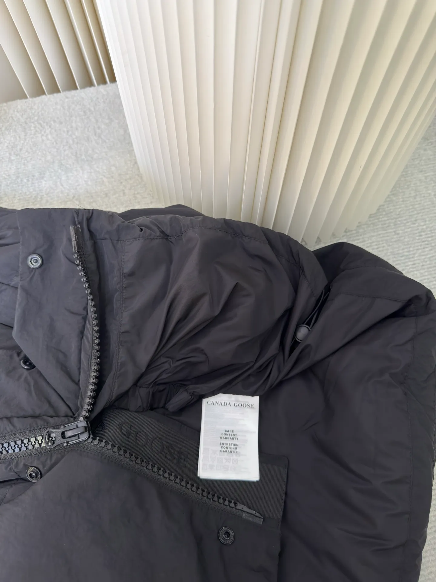 P760 Big Goose Logo Hooded Down Vest is made of high-quality protective nylon fabric, which not only enhances the wear resistance of the surface, but also takes into account wind resistance, ensuring excellent performance in various harsh weather conditions.  90 national standard high-quality white duck down: selected high-loft down, weighing 170g, light and warm, with excellent temperature locking performance and good resilience.  Three-dimensional quilting process: Precision thread reinforcement to prevent velvet drilling and ensure that the fluffy and resilient elasticity lasts as new.  Details: The ribbon is woven with polyester as the base. The brand letters are decorated on the ribbon through high-precision computer embroidery. The edges of the pattern are clear, the stitches are fine and even, and multiple layers of embroidery thread are stacked to enhance the three-dimensional effect. Size S M L XL